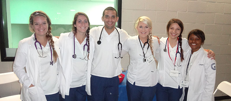 Six smiling Shorter nursing students in white lab coats